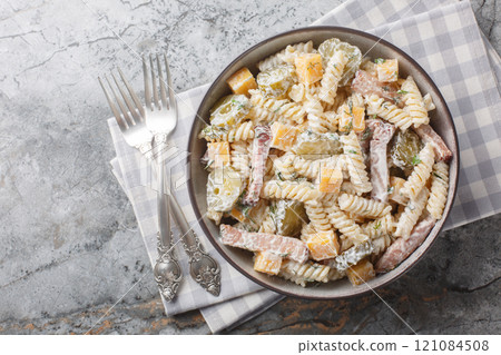 Winter delicious pasta salad with pickles, yellow cheese, herbs and bacon seasoned with mayonnaise close-up in a bowl. Horizontal top view 121084508