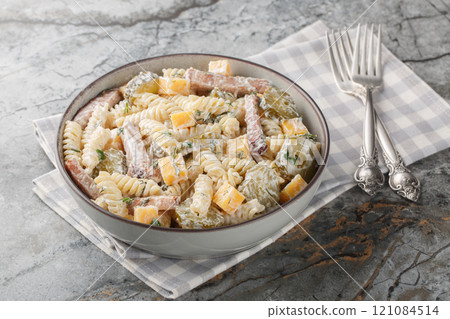 Winter delicious pasta salad with pickles, yellow cheese, herbs and bacon seasoned with mayonnaise close-up in a bowl. Horizontal 121084514