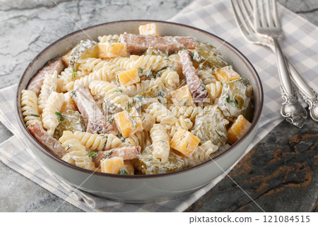 Creamy pickles pasta salad with yellow cheese, herbs and bacon close-up in bowl. Horizontal 121084515