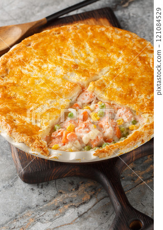Salmon pot pie made from with fresh salmon fillets, mixed vegetables, a creamy sauce and a crisp puff pastry lid closeup on the baking dish. Vertical 121084529