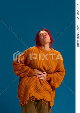 Young caucasian woman with hand on stomach because of menstruation, nausea, painful disease feeling unwell against dark blue background. 121085283