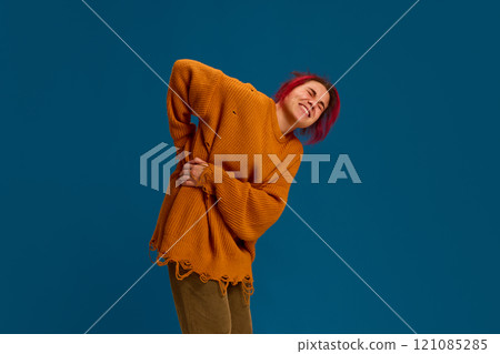 Young woman feeling pain in back and holding ands on spine against dark blue background. Symptoms and treatments. 121085285