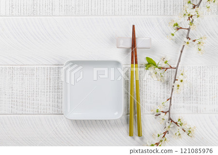 Table adorned with cherry blossom branch and chopsticks, epitomizing Japanese food culture 121085976