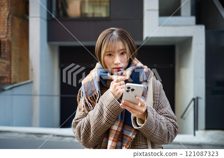 一位身穿冬衣、戴著圍巾、拿著智慧型手機的年輕女子 一位身穿冬衣、戴著圍巾、拿著智慧型手機的年輕女子 121087323