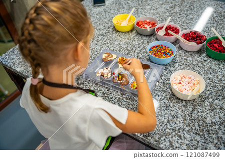 Little girl learning how to cook in a cooking class. Handmade dessert. Making chocolate candy, Child filling heart shaped mold with chocolate Little girl learning how to cook in a cooking class. Handmade dessert. Making chocolate candy, Child filling heart shaped mold with chocolate 121087499