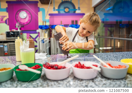 Little girl learning how to cook in a cooking class. Handmade dessert. Making chocolate candy, Child filling heart shaped mold with chocolate Little girl learning how to cook in a cooking class. Handmade dessert. Making chocolate candy, Child filling heart shaped mold with chocolate 121087500