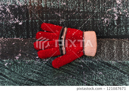 A red glove in the snow, on a wooden background. Christmas background 121087671
