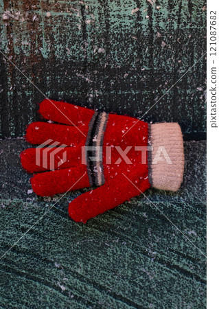 A red glove in the snow, on a wooden background. Christmas background 121087682
