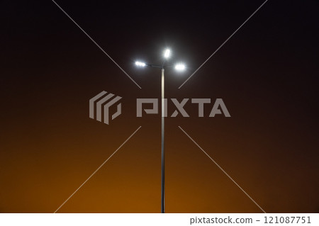 A street lamp in the evening against an orange sky background. Minimalism A street lamp in the evening against an orange sky background. Minimalism 121087751