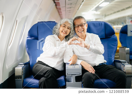 Smiling senior couple of Asian tourists take photos of each other while sitting on a plane. with digital tablet, laptop and smartphone. Travel in style, Smiling senior couple of Asian tourists take photos of each other while sitting on a plane. with digital tablet, laptop and smartphone. Travel in style, 121088539