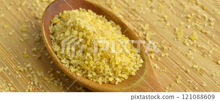 Cracked wheat daliya grains in wooden spoon, on bamboo cutting board 121088609
