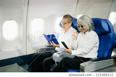 Smiling senior couple of Asian tourists take photos of each other while sitting on a plane. with digital tablet, laptop and smartphone. Travel in style, 121089152