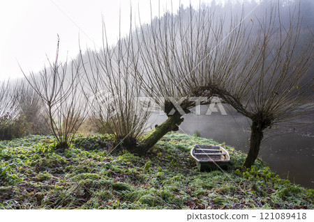 Boat under willow trees in foggy morning, shore of Luznice River, Czech Republic, peaceful relaxation leisure free time or weather forecast concept Boat under willow trees in foggy morning, shore of Luznice River, Czech Republic, peaceful relaxation leisure free time or weather forecast concept 121089418