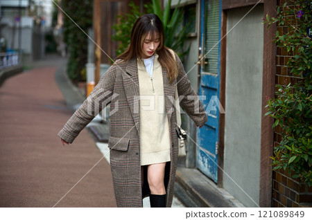 A young woman with long hair wearing a coat taking a walk 121089849