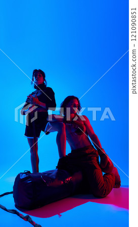 Portrait of shirtless man and woman in sportswear, wearing boxing gloves, posing against blue studio background in neon light. Full-length 121090851