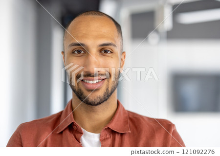 Confident business professional wearing casual orange shirt in modern office setting exuding warmth with genuine smile. Perfect image for themes of professionalism, approachability, and positivity. 121092276