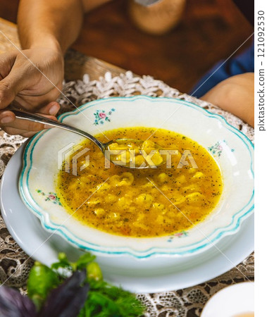 Person eating freshly cooked soup with spoon from floral bowl Person eating freshly cooked soup with spoon from floral bowl 121092530
