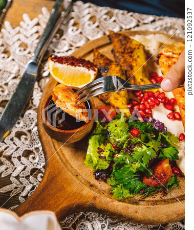 Person enjoying delicious grilled chicken breast with salad on wooden board 121092537