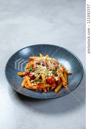 Penne pasta dish with cherry tomatoes and grated cheese being served on a blue plate 121092557