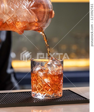 Bartender pouring cocktail into crystal tumbler with ice cubes 121092581
