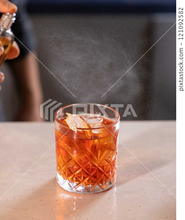 Bartender spraying on cocktail garnish with atomizer in bar setting 121092582