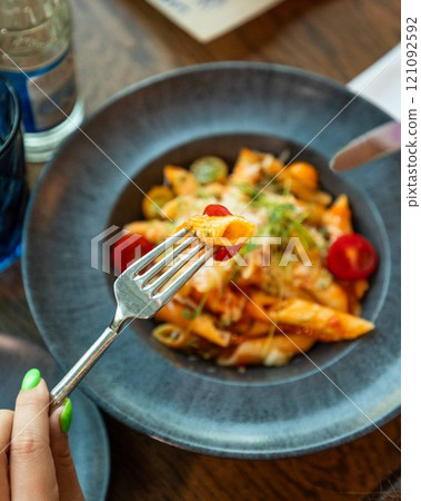 Woman holding penne pasta on fork over plate of food 121092592
