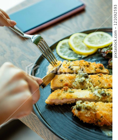 Hands cutting breaded pork cutlets with a metal knife 121092593