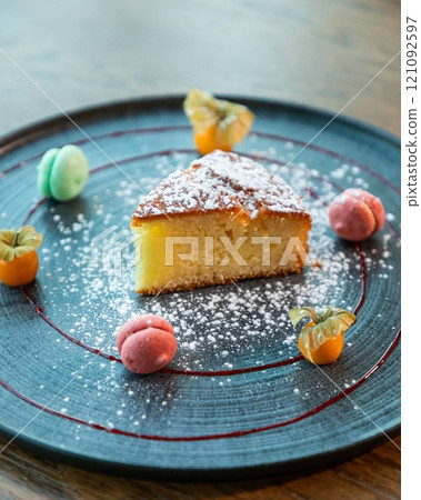 Slice of lemon cake with icing sugar served on a plate with macarons and physalis Slice of lemon cake with icing sugar served on a plate with macarons and physalis 121092597