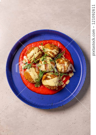 Breaded chicken croquettes served on tomato sauce with microgreens and creamy sauce on blue plate 121092611