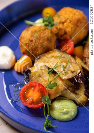 Arancini being served on blue plate with eggplant and tomatoes Arancini being served on blue plate with eggplant and tomatoes 121092624