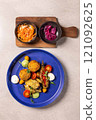 Top view of a vegetarian meal with fried vegetables and fritters served on a blue plate with pickled carrots and onions on the side 121092625