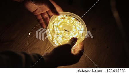Woman holding a skein of garland with warm lights close up. Atmosphere for Christmas celebration. Woman holding a skein of garland with warm lights close up. Atmosphere for Christmas celebration. 121093331