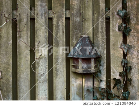 An old creepy wooden fence on a summer day in a remote village. A spooky barricade on a Halloween morning with a chilling feel. An eerie barrier with a strange antique rustic birdhouse on it 121094040