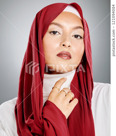 Portrait of a Muslim woman wearing a red hijab or headscarf showing her eyelash extensions and makeup. Showing her flawless skin glowing. Beautiful woman isolated against a grey studio background. Portrait of a Muslim woman wearing a red hijab or headscarf showing her eyelash extensions and makeup. Showing her flawless skin glowing. Beautiful woman isolated against a grey studio background. 121094084