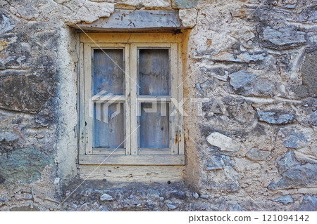 Closeup of a wooden window in a stone wall of an old grey house. Boarded up square window frame in a historic rustic building. Architecture and background of a rural structure outside with copyspace 121094142