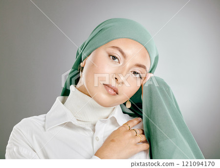Studio portrait of beautiful muslim woman isolated against a grey background. Young woman wearing hijab or headscarf showing traditional arab modesty holding her hands together and looking at camera 121094170