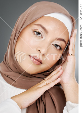 Portrait of a glowing elegant muslim womans face isolated against grey studio background. Young woman wearing a hijab or headscarf, showing her eyelash extensions, jewellery and skin routine 121094258