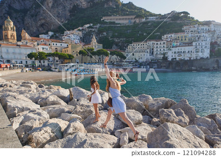 Friends, women and holiday on rocks at beach for travel, vacation adventure and bonding with freedom. People, jumping and exploring destination for sightseeing together outdoor in nature in Italy 121094288