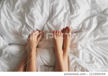 Legs, women and friends in bed at home in morning on sleepover for bonding and relax. People, girls and rest with manicures in bedroom for love, conversation and comfortable on break as roommates 121094344