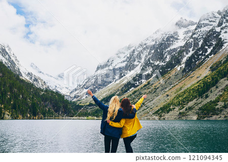 Women, friends and open arms in lake on mountain with snow for winter holiday and adventure. Back view, tourist and freedom in water dam at countryside for hiking, camping and bonding in Canada Women, friends and open arms in lake on mountain with snow for winter holiday and adventure. Back view, tourist and freedom in water dam at countryside for hiking, camping and bonding in Canada 121094345