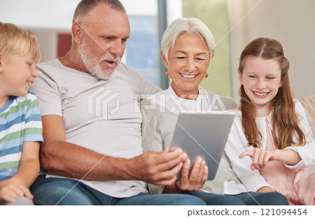 A happy mature couple bonding with their grandchildren while babysitting and using a digital tablet at home. Grandparents relaxing with their cute little grandson and granddaughter browsing internet 121094454