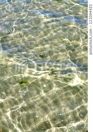 Above view of sunlight reflecting on water at beach. Closeup of shallow waves and calm ripples on coastline on sunny day outside. Clear liquid refracting sun rays in summer for copy space background 121094483