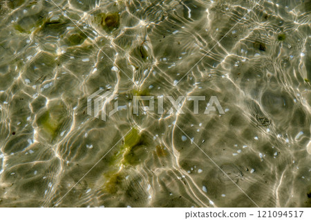 Clear beach water on a summer day with copy space. Top view of calm low tide sea ripples during spring. Closeup of the bright sun reflection shining off the shallow ocean useful as a background 121094517