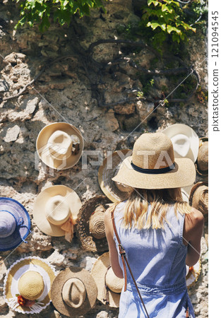 Woman, back and shopping for hat at street market in summer, outdoor and search for deal on vacation. Person, customer and choice in village with fashion, clothes and discount on road in Italy 121094545