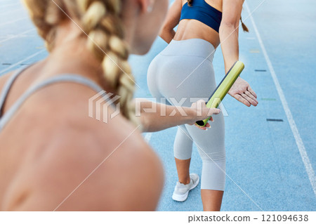 Relay race athlete handing the baton over to a teammate while running from behind. Rearview closeup of two female athletes working together as a team to compete in and win a sports competition 121094638