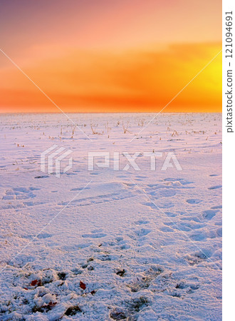 Snow covered fields at orange sunset. Stunning orange sky on empty frozen farmland. Winter landscape scene of soft fresh white snowfall at dawn in an arctic scene. Global warming and climate change. 121094691