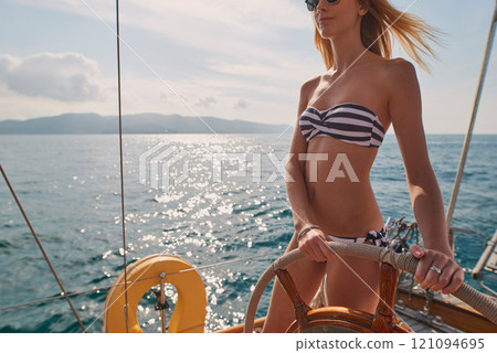 Woman, bikini and yacht with hands on steering wheel, outdoor and travel in sunshine on ocean. Girl, boat and summer with swimwear, direction and control on cruise, holiday and journey in Italy 121094695