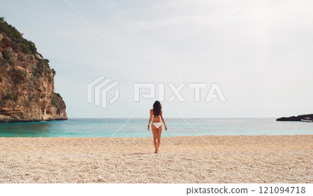 Rear view, woman and bikini on beach in summer for holiday, vacation or swimming with sky and rock. Person, walking and swimwear on sand by ocean or sae for relax, peace and freedom outdoor in nature Rear view, woman and bikini on beach in summer for holiday, vacation or swimming with sky and rock. Person, walking and swimwear on sand by ocean or sae for relax, peace and freedom outdoor in nature 121094718