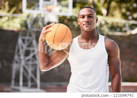 Portrait of a young black male basketball player holding a ball, playing a match on a local sports court outside. One cool muscular man with attitude taking a break to play a fun recreational game 121094741