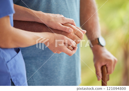 A nurse and senior patient holding hands while helping him to walk outside. Closeup of an elderly man being supported by female caregiver while walking to improve his mobility, health, and wellbeing 121094800